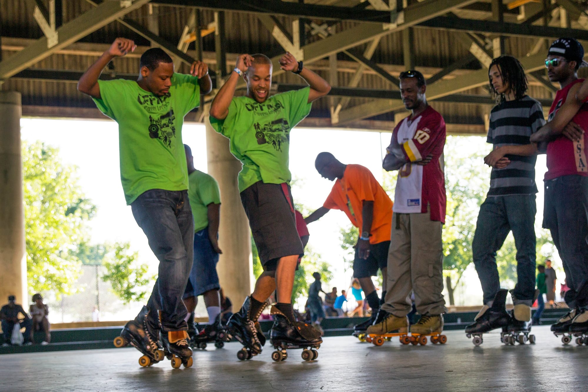 Two people in green shirts do a synchronized roller skating trick.