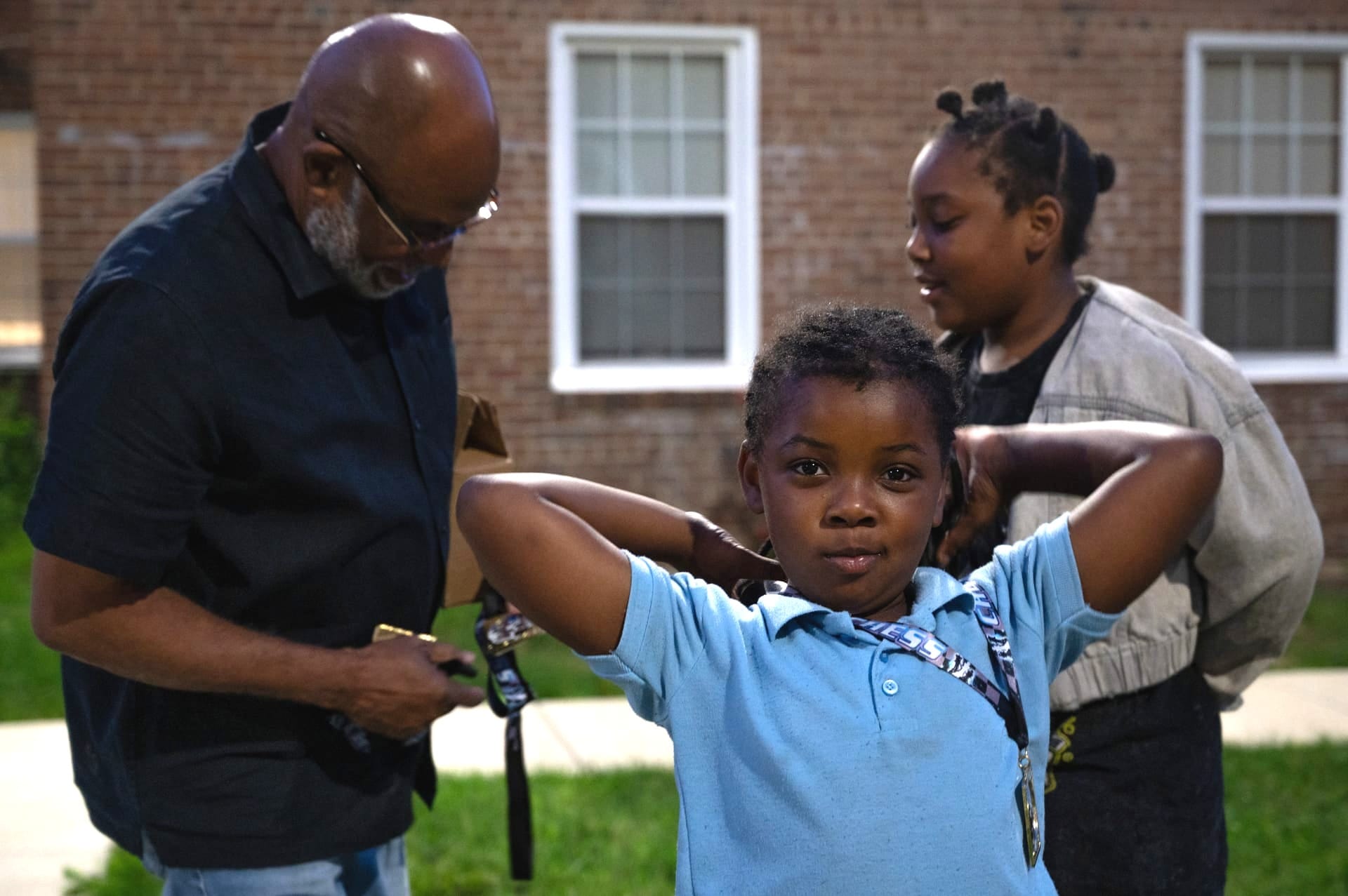 A young girl in a blue shirt wears a chess medal in the foreground. Vaughn Bennett is seen giving a medal to her older sister in the background.