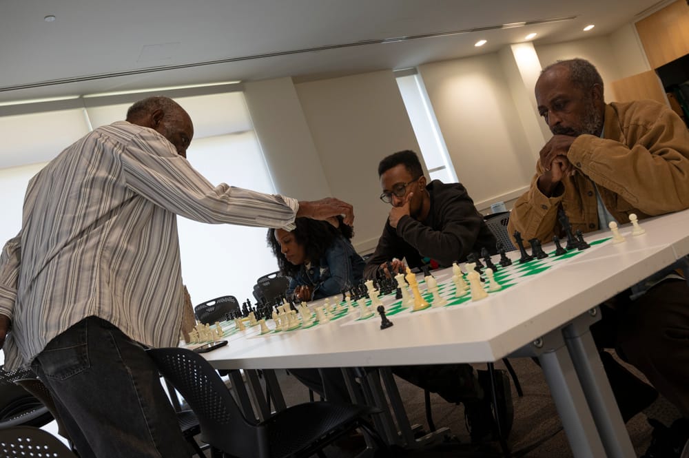 Adults at a chess class are seen before chess boards, considering their next moves.