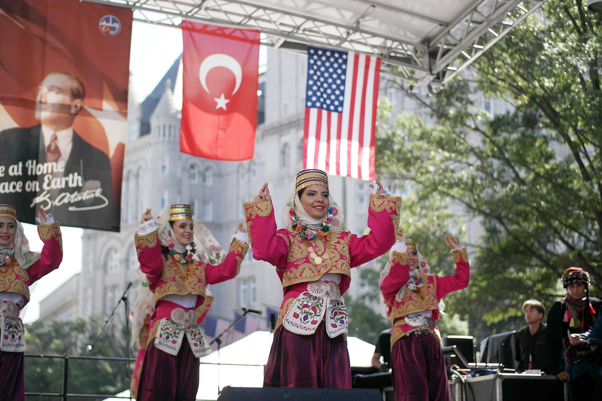 Dancers on a stage wearing colorful costumes, in front of flags from Turkey and the U.S.