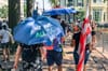 A person walking with a blue umbrella that reads We Are All DC, next to a person with a DC flag. 