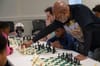 Vaughn Bennett leans over a chess board, teaching kids at a table how to play the game.